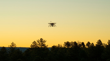 A drone flying over the treeline during sunset