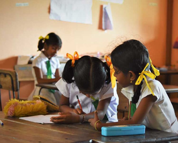 Children sit behind a desk in a classroom writing