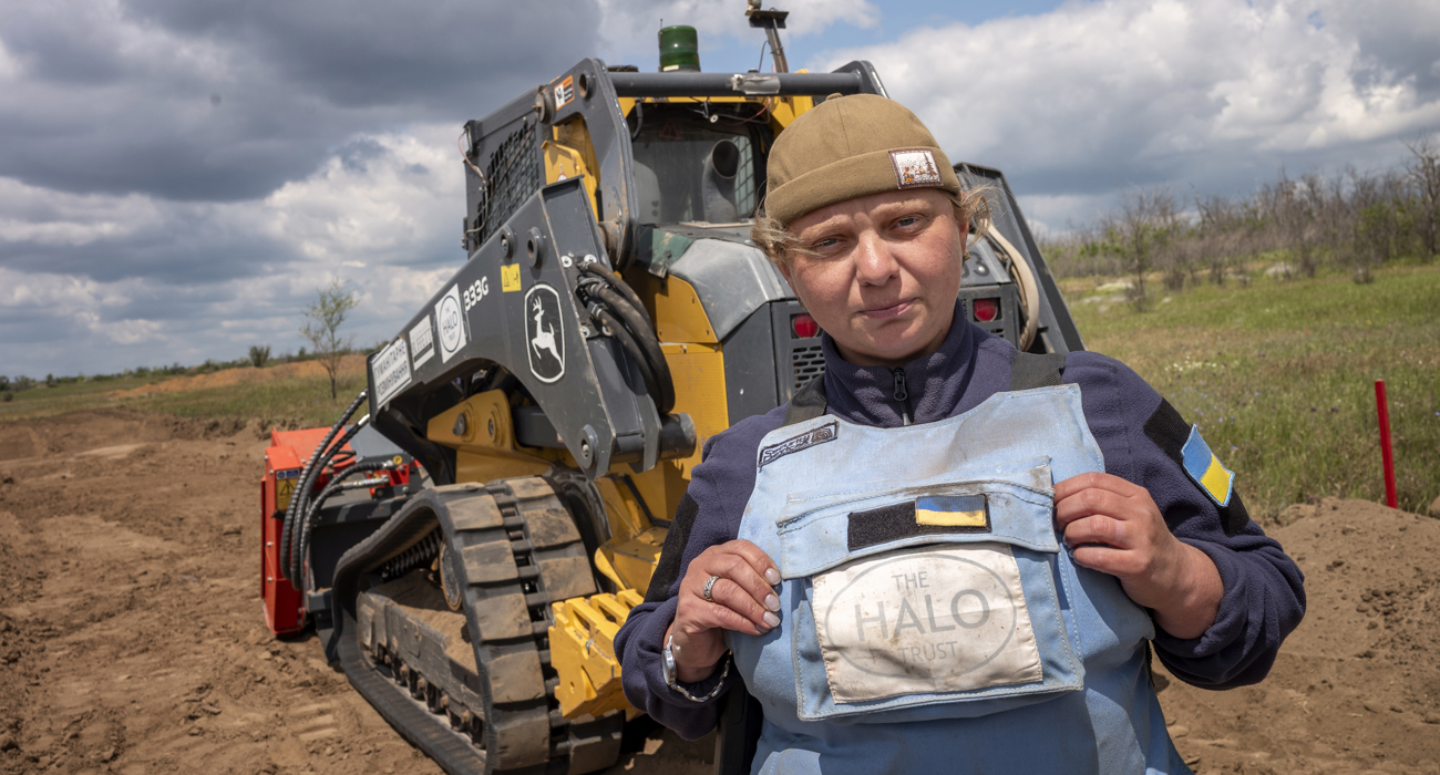 A woman in a HALO Trust vest stands in front of a bulldozer.