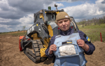 A woman in a HALO Trust vest stands in front of a bulldozer.