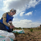 HALO staff member wearing protective gear holds a wire while kneeling on sandbags