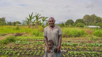 A man and his young son stand in front of their green garden