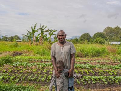 A man and his young son stand in front of their green garden