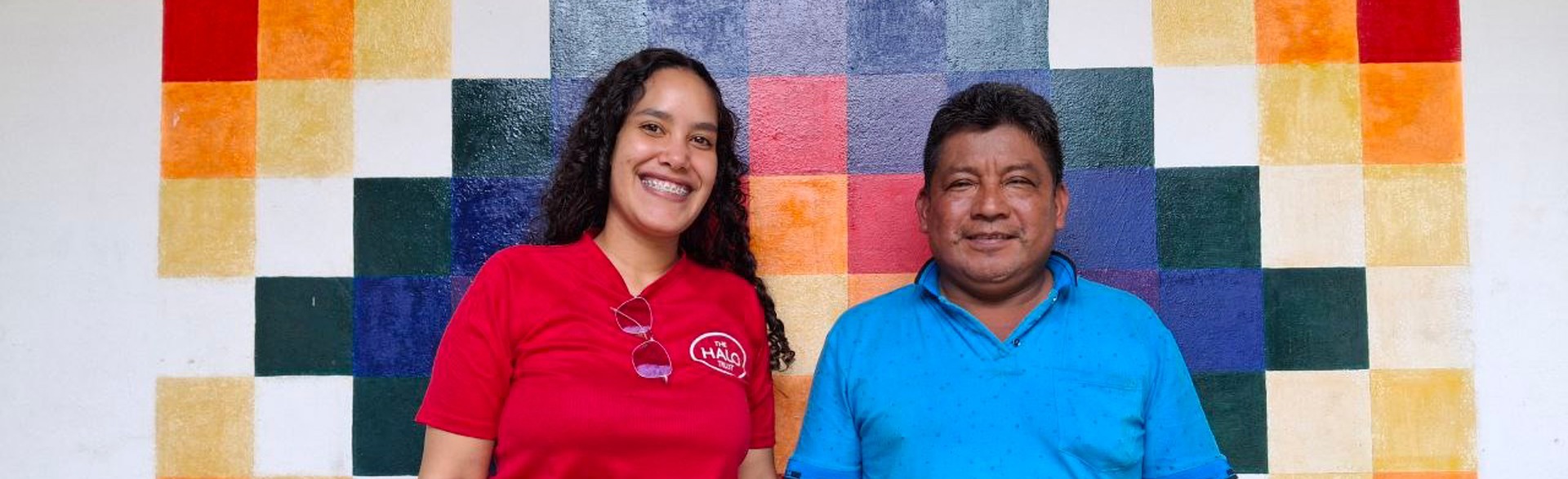 A woman in a red polo and man in a blue polo stand before a geometric mural.