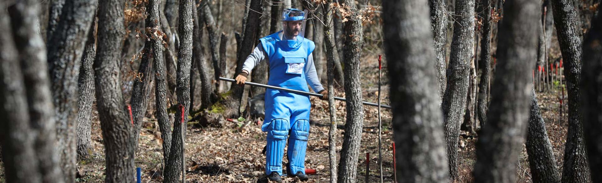 A deminer wearing PPE marks mines in the forest