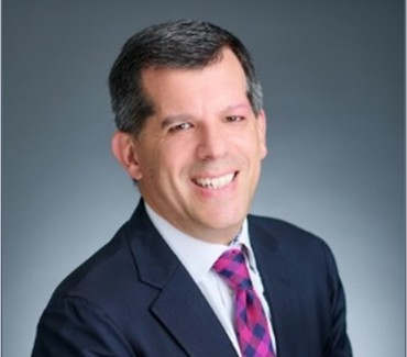 Fred Turner, smiling and posing for a portrait in front of a gray background