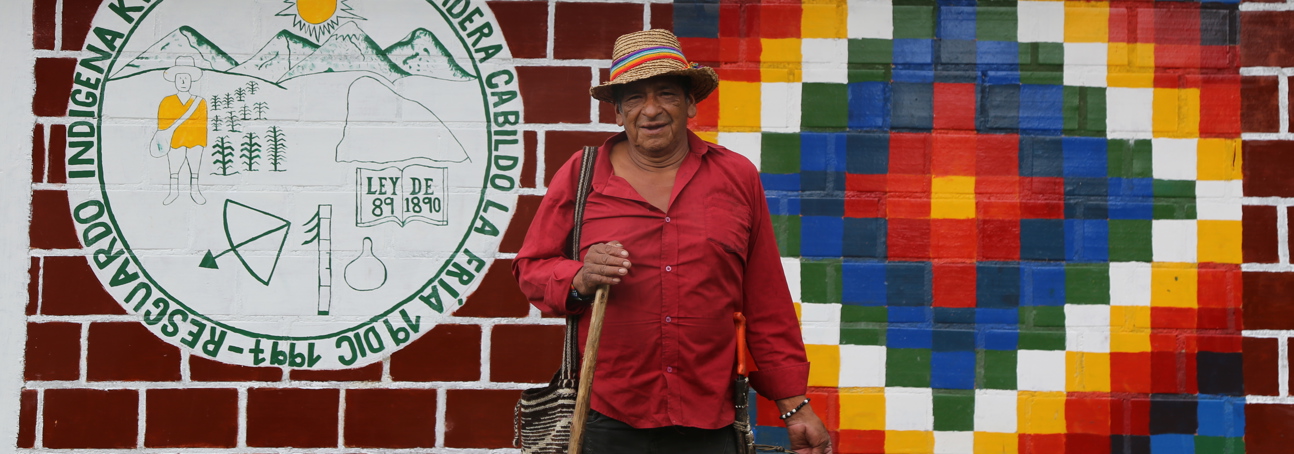 Luis Ángel, an Elder from Kwet Wala Indigenous Reservation poses in front of a painted  building