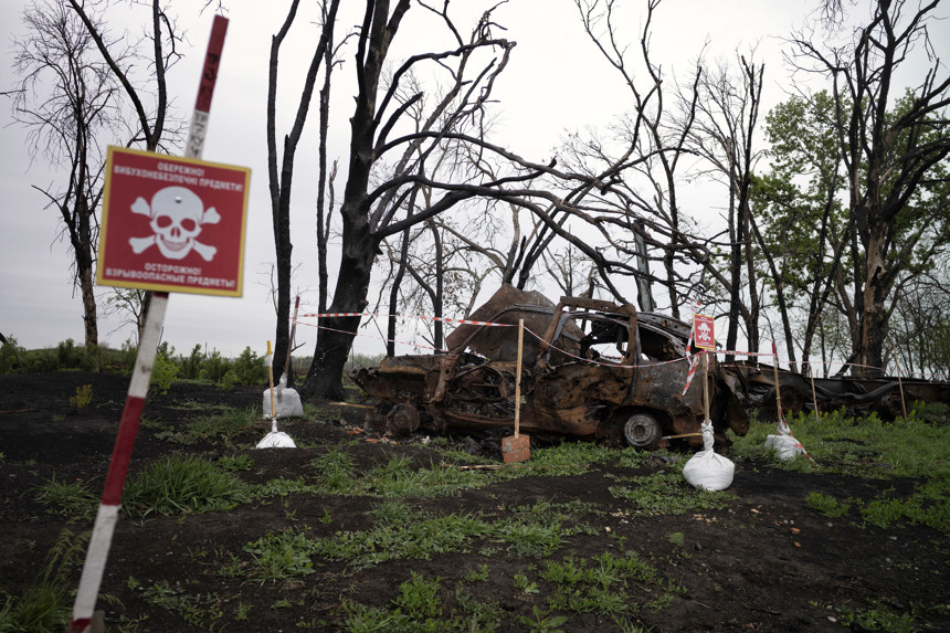 A rusting vehicle sits in a mine marked field with warning signs