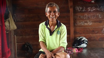 Ouk, a farmer from Cambodia smiles while sitting on a bench