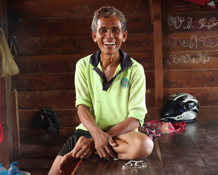 Ouk, a farmer from Cambodia smiles while sitting on a bench