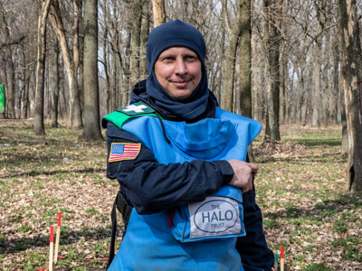 Ukraine deminer shows the US badge on his arm while standing in a forest with mine markers