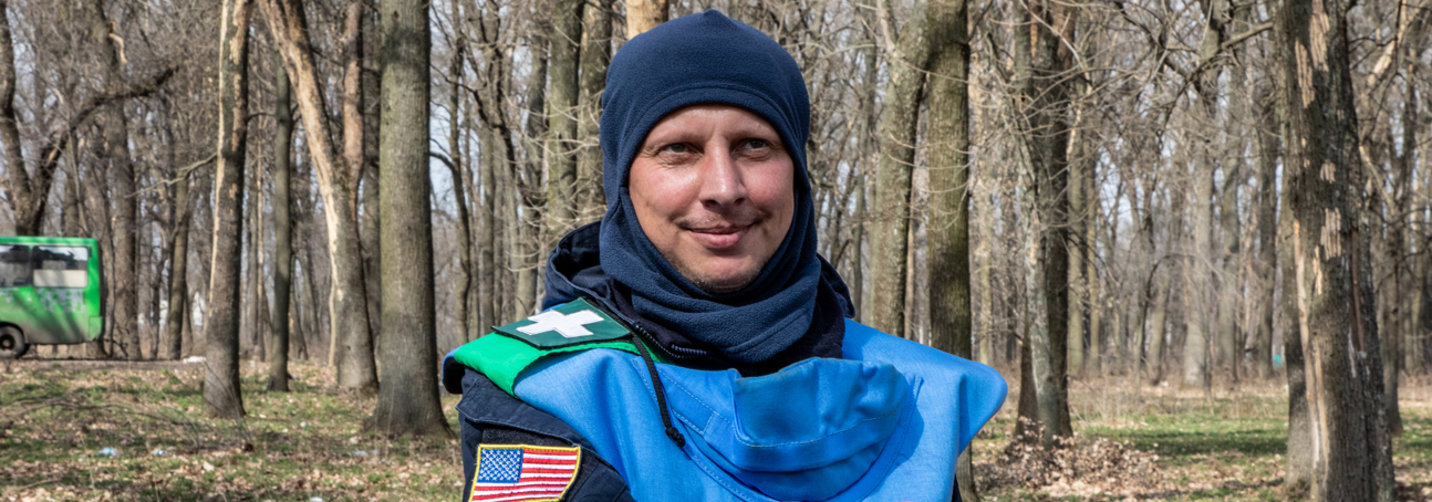 Ukraine deminer shows the US badge on his arm while standing in a forest with mine markers