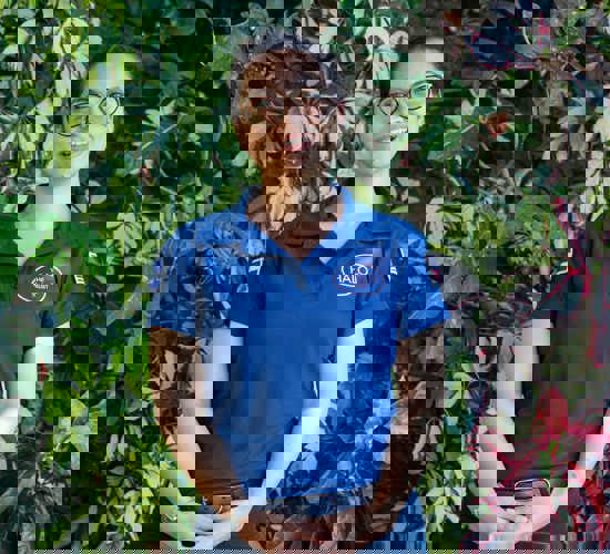 Lisseth wears a HALO polo shirt, standing in front of green and pink plants