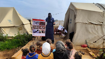 Kids sit on a rug outside listening to a HALO risk educator 