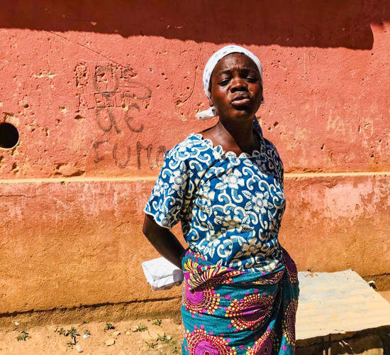 Rufina Chipanda, a local parent, stands in front of a concrete building with her hands behind her back