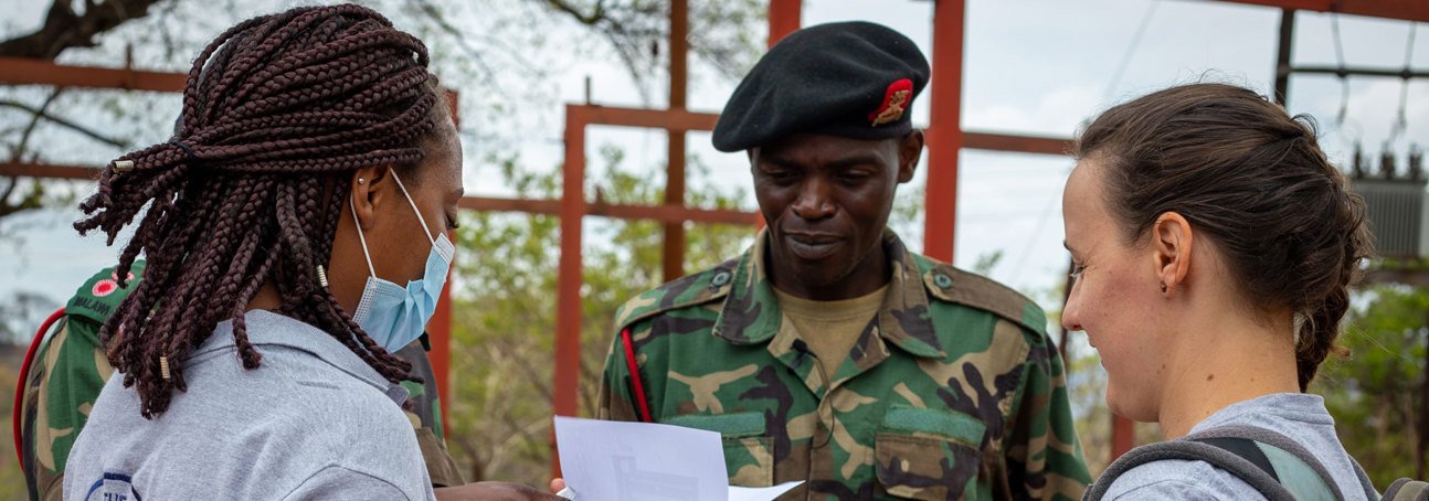 HALO staff members look at a piece of paper with military personnel outside