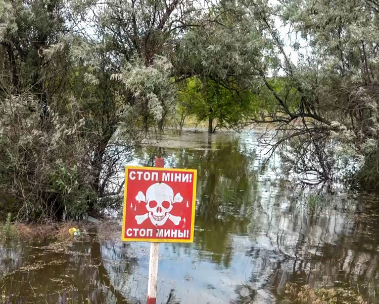 A red danger mines sign stands in front of the destruction of the Kakhovka Dam Flood