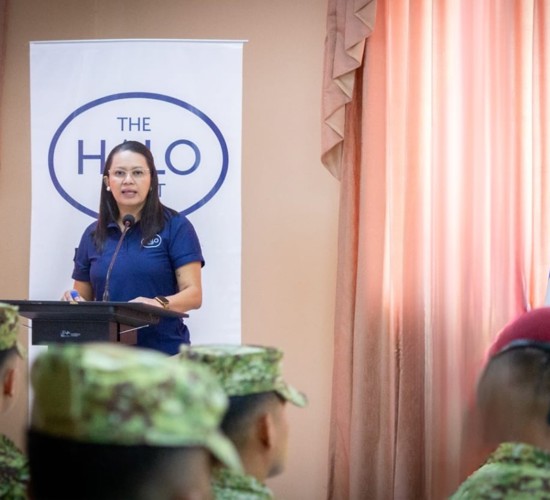 Deysi stands at a lectern wearing a HALO top in front of military personnel