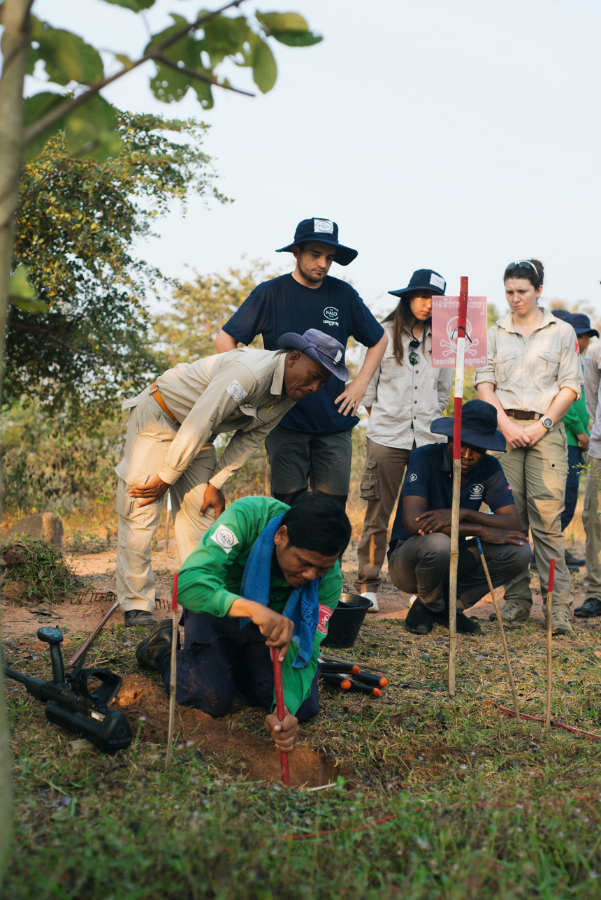 Un Ek and colleagues watch over fellow HALO staff digging in a mine marked area
