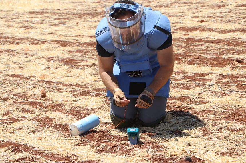 A deminer wearing PPE works with wires on the ground