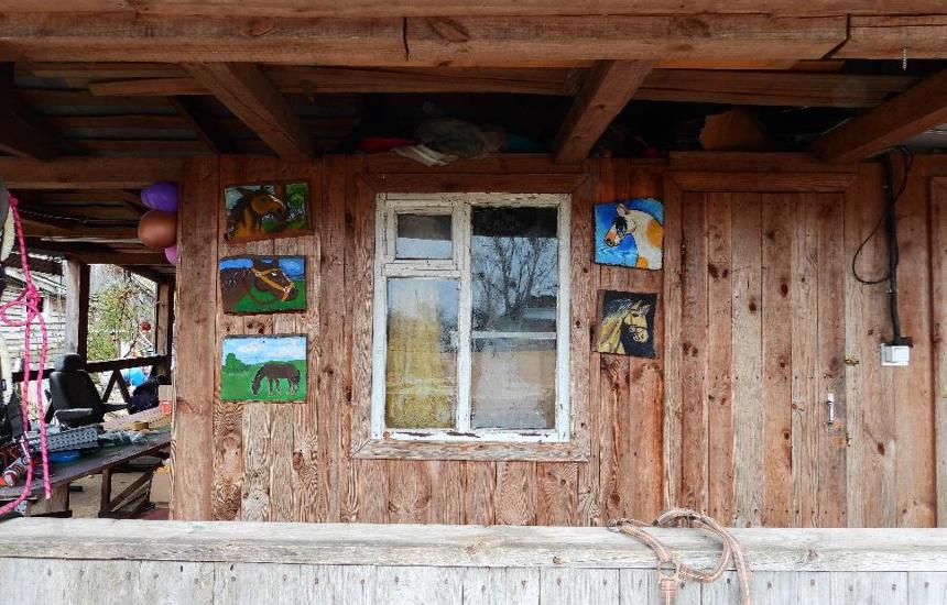 Children's paintings of horses hung around a window on a wall outside