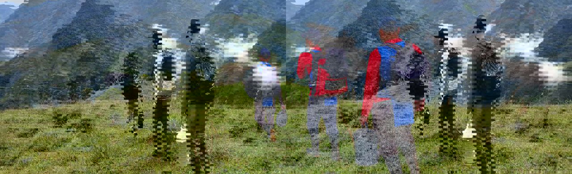 Three deminers walk through a field with mountains surrounding them