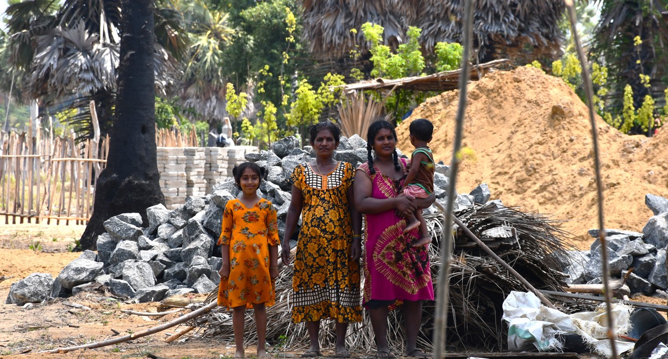 Two women, a young girl, and a toddler in colorful dresses stand in front of a pile of rocks.