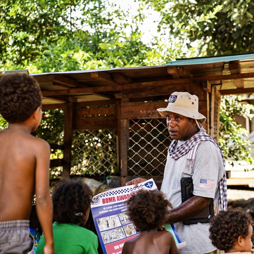 A HALO staff member holds a poster about bomb awareness as he gives a risk education session to kids outside
