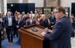 A man stands at the event podium speaking to a full room