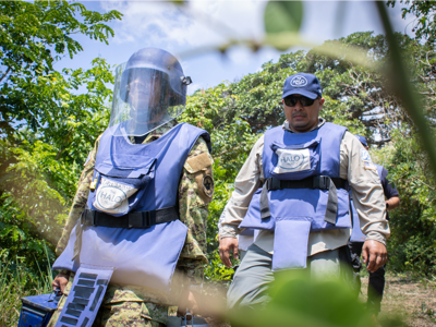 Captain Flores, wears PPE and walks through a forest with a HALO technician
