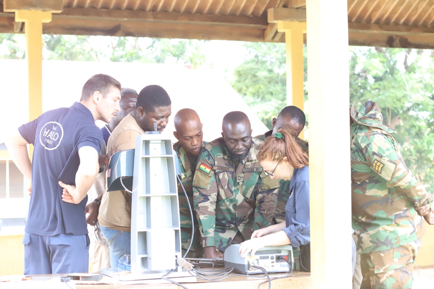 Military personnel stand around HALO staff members using a weapons marking machine