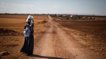 Deminer Hiba talks on a portable radio in front of a long stretch of dirt road.