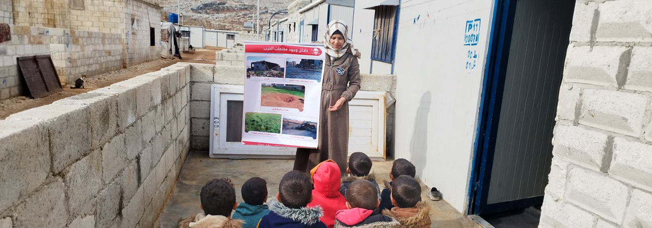 Kids sit in the front yard of a building listening to a HALO risk educator 