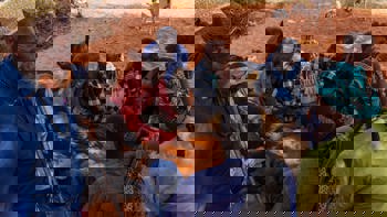 Group of Somaliland men sitting on the orange tinted soil play a game with date stones