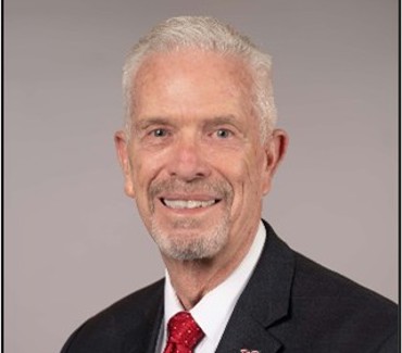Bill Johnson, smiling and posing for a portrait in front of a neutral background