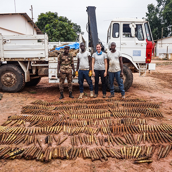 HALO staff members and a military personnel stand in front of many obsolete ammunitions on the ground