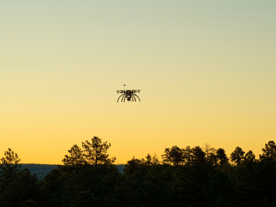 A drone flying over the treeline during sunset