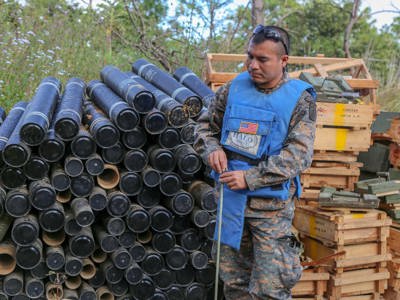 A deminer stands in front of crates and cylinder containers outside