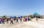 Parishioners walk across the sandy land in front of the bright blue church